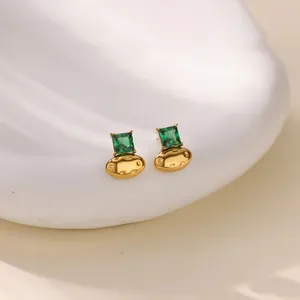 Dettaglio di orecchini a perno dorati con pietre di zircone verde smeraldo quadrato.