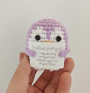 Close-up view of a handmade purple crochet penguin holding a positive message card