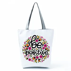 Close-up of a white tote bag featuring a vibrant floral pattern and 'be positive' text