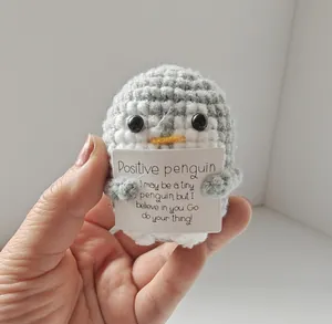 Handmade crocheted penguin doll holding a motivational positive card for gift decoration.
