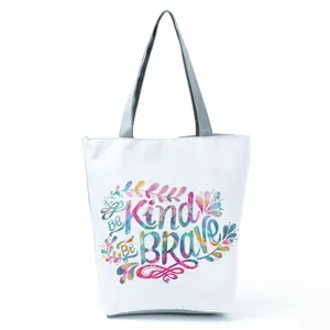 Detailed view of a white tote bag featuring colorful 'Be Kind Be Brave' floral typography.