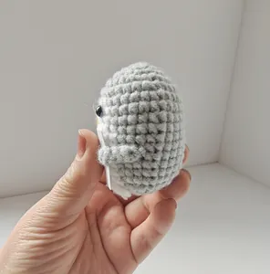Close-up of a handmade gray crochet penguin plush being held to show knitted texture