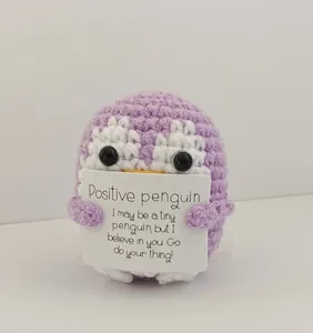 Detailed view of handmade crochet purple penguin holding a positive motivational card