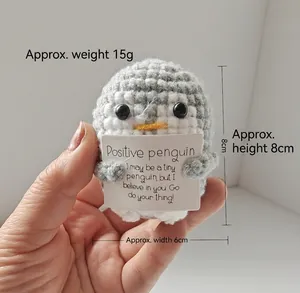 Close-up detail of handmade crochet positive penguin toy holding a motivational card