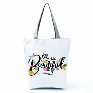 Detailed view of the white tote bag with floral print and 'You are Beautiful' text.