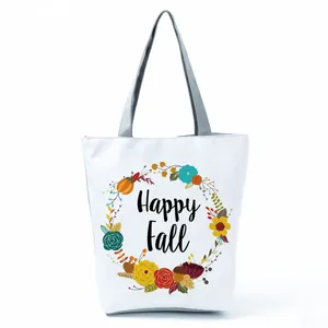 Close-up detail of a white canvas tote bag featuring a floral wreath and Happy Fall text