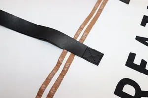 Close-up detail of sturdy black strap and reinforced stitching on white canvas tote bag.