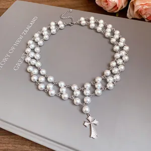 Elegant double strand pearl necklace featuring a detailed zircon cross pendant on a book cover