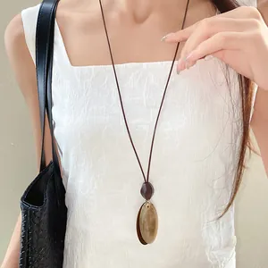 Detailed close-up of a vintage irregular oval pendant necklace with a brown wax cord.
