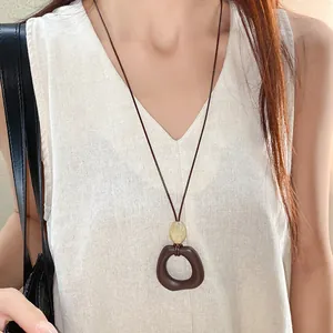 Close-up of irregular oval pendant on a brown wax cord necklace with a yellow bead