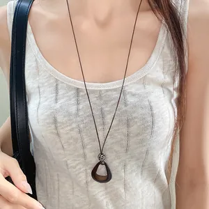 Close-up detail of an irregular dark oval pendant necklace with a brown wax cord