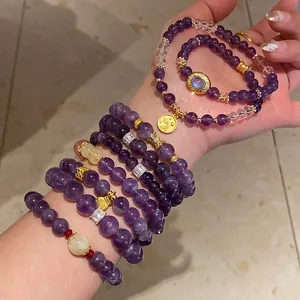 Detalle de pulseras de cuentas de amatista púrpura apiladas con dijes y colgantes dorados
