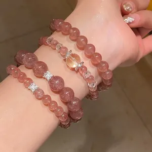 Detalle de pulseras de cristal de cuarzo fresa y cuarzo fantasma púrpura en una muñeca.