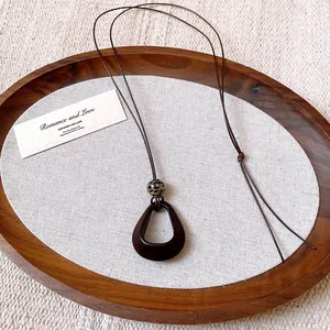 Detail view of a retro irregular dark oval pendant necklace on a brown wax rope.