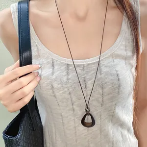 Detail shot of a vintage irregular oval pendant necklace worn on a brown wax cord.