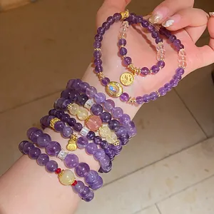 Pila de pulseras de cuentas de amatista y cuarzo fresa con amuletos dorados en la muñeca.