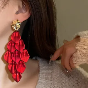 Detail view of oversized red petal tassel earrings with gold stud worn by model.