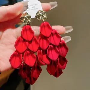 Close-up detail of oversized red petal tassel earrings with textured gold studs.