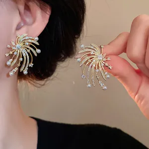 Detailed view of fireworks-shaped earrings with zircon stones and pearls on an ear.