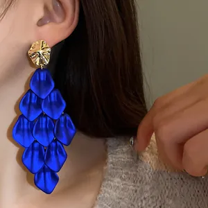 Close-up view of bold cobalt blue petal tassel earrings with gold studs worn by a model