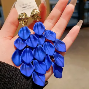 Close-up detail of oversized blue matte petal tassel earrings with gold geometric studs