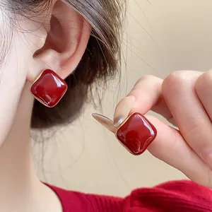 Close-up detail of vintage red square enamel stud earrings with gold trim on ear