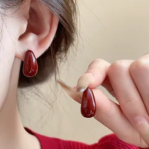 Close-up view showing elegant deep red teardrop-shaped earrings with glossy enamel finish