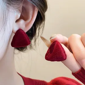 Macro view of red flocked triangular earrings worn on ear and held by hand