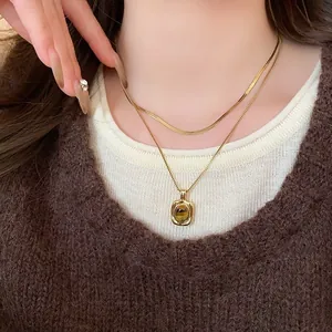 Dettaglio di collane sovrapposte placcate oro con pendente vintage in occhio di tigre.
