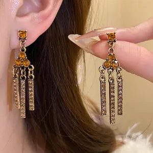 Close-up of elegant vintage-style drop earrings featuring amber rhinestones and gold bars.