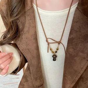 Primo piano di una collana retrò con ciondolo a fungo e perline occhio di tigre su cordino.