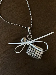 Detailed view of woven bag and heart pendants with white bow on a silver ball chain