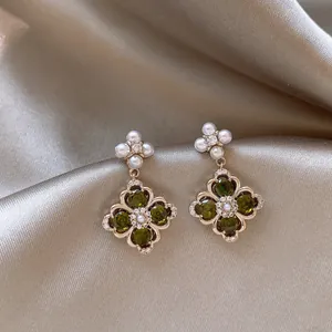 Detailed view of green zircon stones and pearl floral accents on vintage gold earrings