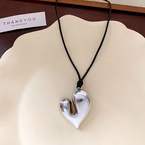 Élégant collier avec pendentif coeur argenté et cordon noir sur une assiette en céramique.