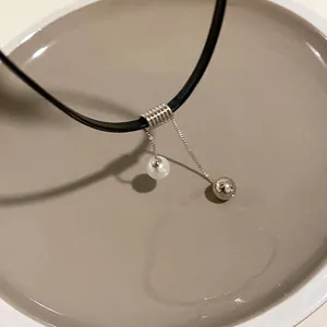 Dettaglio di un choker in pelle nera con ciondolo a perla e sfera d'argento su vassoio