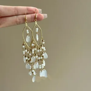 Close-up of bohemian gold tassel earrings with white glass beads and teardrop pendants