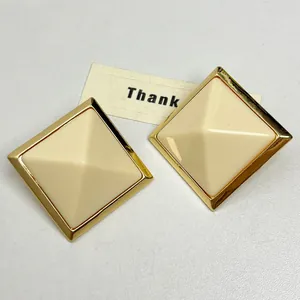 Close-up of minimalist cream resin pyramid stud earrings with elegant gold-toned frame