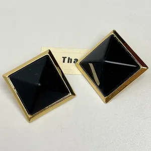 Close-up detail of black resin rhombus stud earrings featuring a gold-plated frame