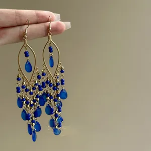 Close-up of Bohemian earrings with blue glass beads and teardrop tassels on gold hooks.