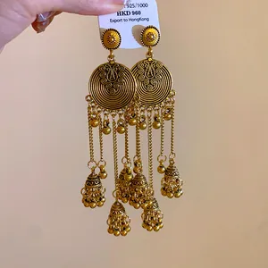 Close-up of vintage ethnic gold tassel earrings with bell charms and silver needles.