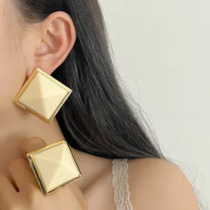 Close-up of minimalist geometric cream resin stud earrings with elegant gold-toned metal frame.