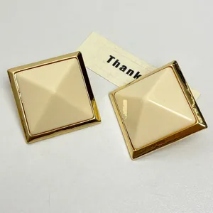 Macro view of beige square resin stud earrings with gold metal frame and pyramid design
