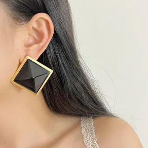 Close-up detail of a minimalist black resin diamond stud earring on an Asian model's ear