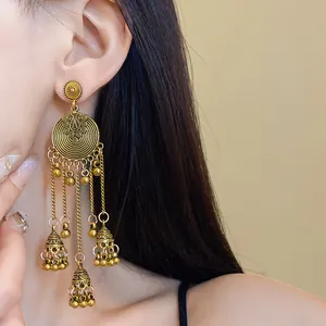 Detail view of ethnic style vintage golden copper bell tassel earrings worn by model