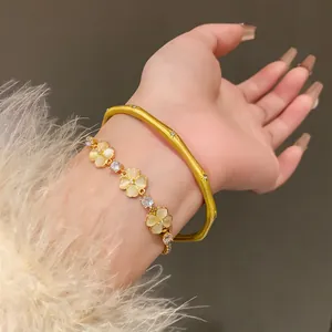 Close-up detail of an elegant gold-tone flower bracelet and bamboo-style bangle on a wrist