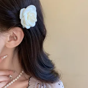 Detailed close-up shot of an elegant white rose hair clip styled on dark wavy hair
