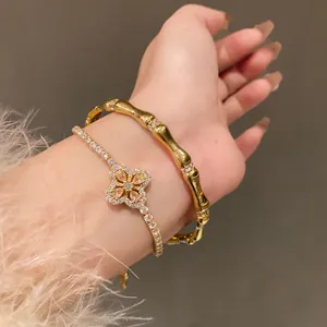 Close-up of elegant gold bamboo bangle and sparkling zircon flower bracelet on a wrist.