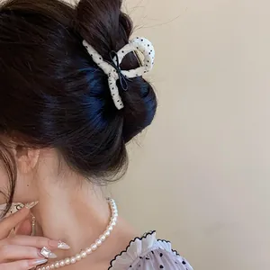 Close-up of a white polka dot hair claw clip with a black bow on a bun.