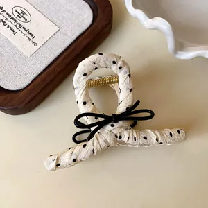 Close-up of cream polka dot fabric wrapped hair claw clip with a black bow accent