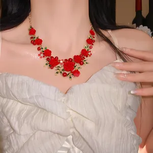 Detail view of a sweet pastoral style necklace featuring red roses and green leaf accents